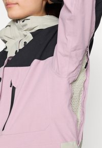 Hoodie-Jacke in Schwarz, Hellgrau und Pastellrosa. Mit Netzfutter, Reißverschluss-Seitenschlitzen und vorderen Taschen mit Knopfverschlüssen.