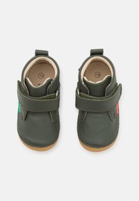 Chaussures pour bébé en cuir vert avec une sangle Velcro, des orteils arrondis et une doublure intérieure beige. Comprend de petites étiquettes rouges et vertes. Taille 19.