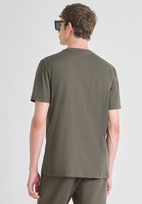 Camiseta de algodón verde olivo con mangas cortas, cuello redondo y una textura suave, vista desde la parte de atrás, combinada con gafas de sol negras.