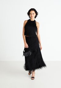 Black two-piece outfit featuring a sleeveless cropped top and a long skirt with a textured, fringed finish; paired with a small black handbag.
