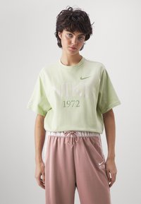 Světle zelené bavlněné tričko s velkým nápisem "NIKE" a "1972" pod ním. Má krátké rukávy a klasický kulatý výstřih.