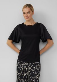 Czarna bluzka z krótkimi, falbanowymi rękawami i okrągłym dekoltem z subtelnym metalicznym akcentem. Gładka tekstura, lekki materiał.