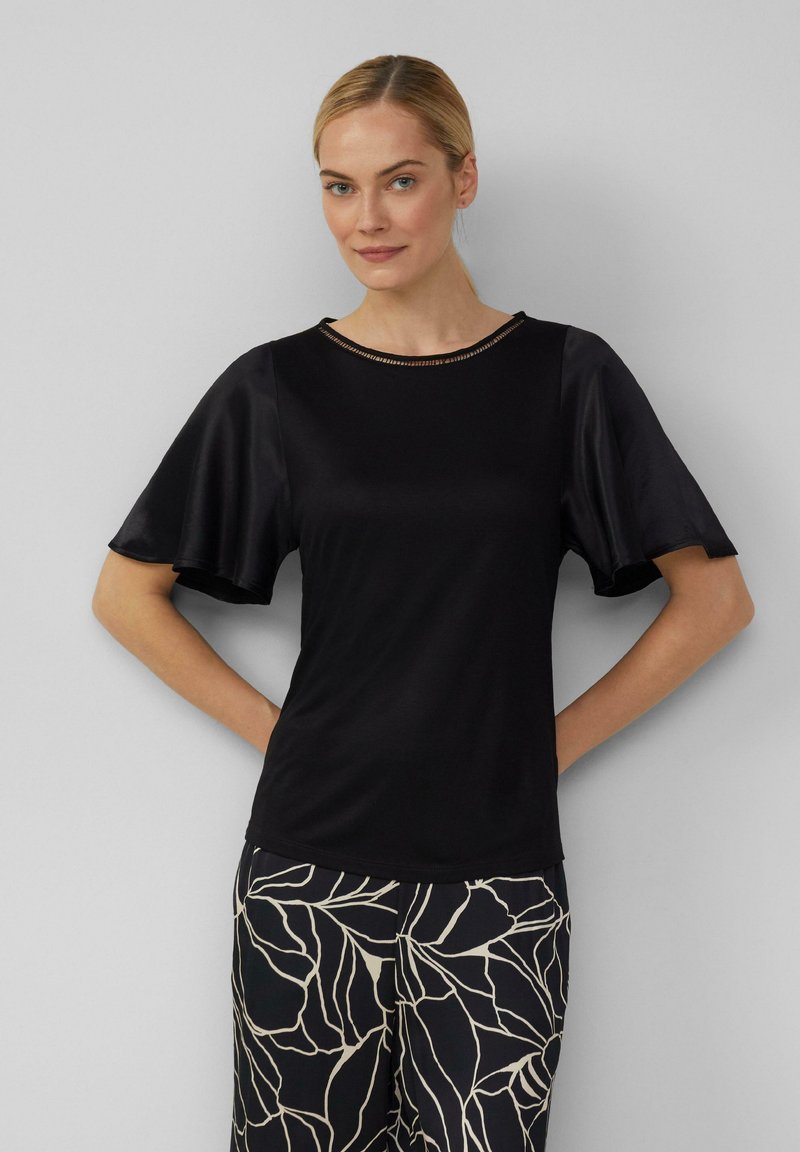 Czarna bluzka z krótkimi, falbanowymi rękawami i okrągłym dekoltem z subtelnym metalicznym akcentem. Gładka tekstura, lekki materiał.