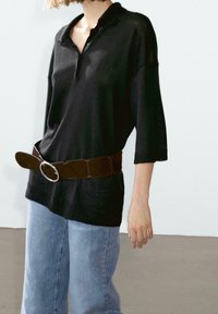 Person wearing loose black knit sweater with three-quarter sleeves, wide brown belt with round buckle, and light blue denim jeans.