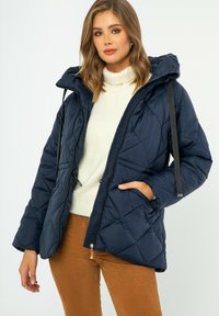 Návlečný prošívaný puffer kabát v námořnické barvě s kapucí, předním zipem a šnůrkou. Obsahuje boční kapsy a texturovaný design látky.