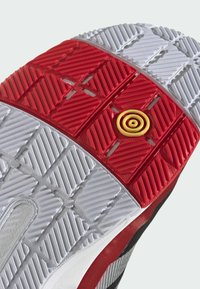 Rød og grå gummisko sål med et tekstureret design, der har forhøjede mønstre og en gul cirkulær detalje i midten.