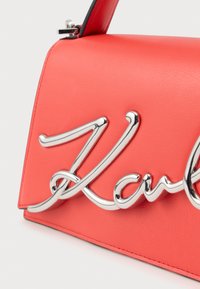 Rode leren handtas met grote glanzende zilveren tekstdetails en een sluiting aan de bovenkant.