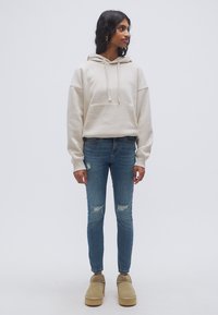 Μπεζ φούτερ με κουκούλα και μπροστινή τσέπη, σε συνδυασμό με καταπονημένο στενό τζιν μπλε χρώματος και μπεζ παπούτσια με πλατφόρμα. Απλός σχεδιασμός, άνετη εφαρμογή.