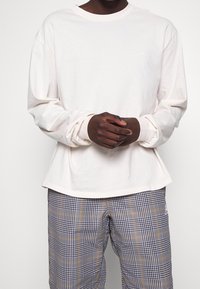 Light beige long-sleeve shirt with a crew neckline and elastic cuffs, paired with checkered pants featuring navy, white, and yellow patterns.
