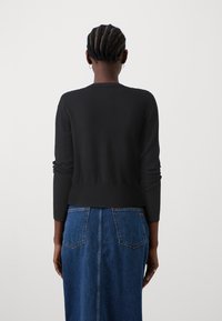 Svart strikket genser med lange ermer, tettsittende stil og ribbestrikket kant. Kombinert med et høyt liv blått denimskjørt med baklommer.