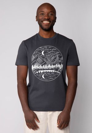 Dunkelgraues Baumwoll-T-Shirt mit einem weißen, kreisförmigen Grafik von Bergen, Bäumen und einem Mond, verziert mit detaillierten Linienstiftakzenten.