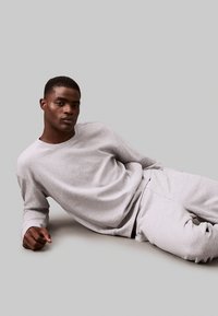 Grijze katoenen sweatshirt en joggers, ontspannen pasvorm met lange mouwen, ronde hals en subtiele geborduurde logo. Soepele textuur, minimalistisch ontwerp.