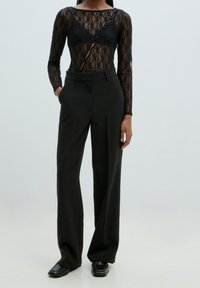 Body en dentelle noire à manches longues, avec un décolleté plongeant et des boutons décoratifs, associé à un pantalon noir taille haute.