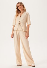 Beige twee-delige outfit met een korte mouwen wikkeltop met een strik en wijde broek in een lichte, getextureerde stof.