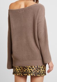 Hnědý pletený svetr s off-shoulder designem, žebrovanými manžetami a spodním lemem; nošený přes zlatou a černou mini sukni s leopardím potiskem.
