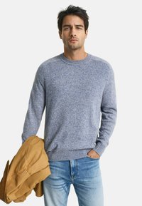 Blauer Pullover mit strukturiertem Muster. Runder Ausschnitt, gerippte Bündchen und Saum. Getragen mit hellblauen Jeans und einer braunen Jacke.