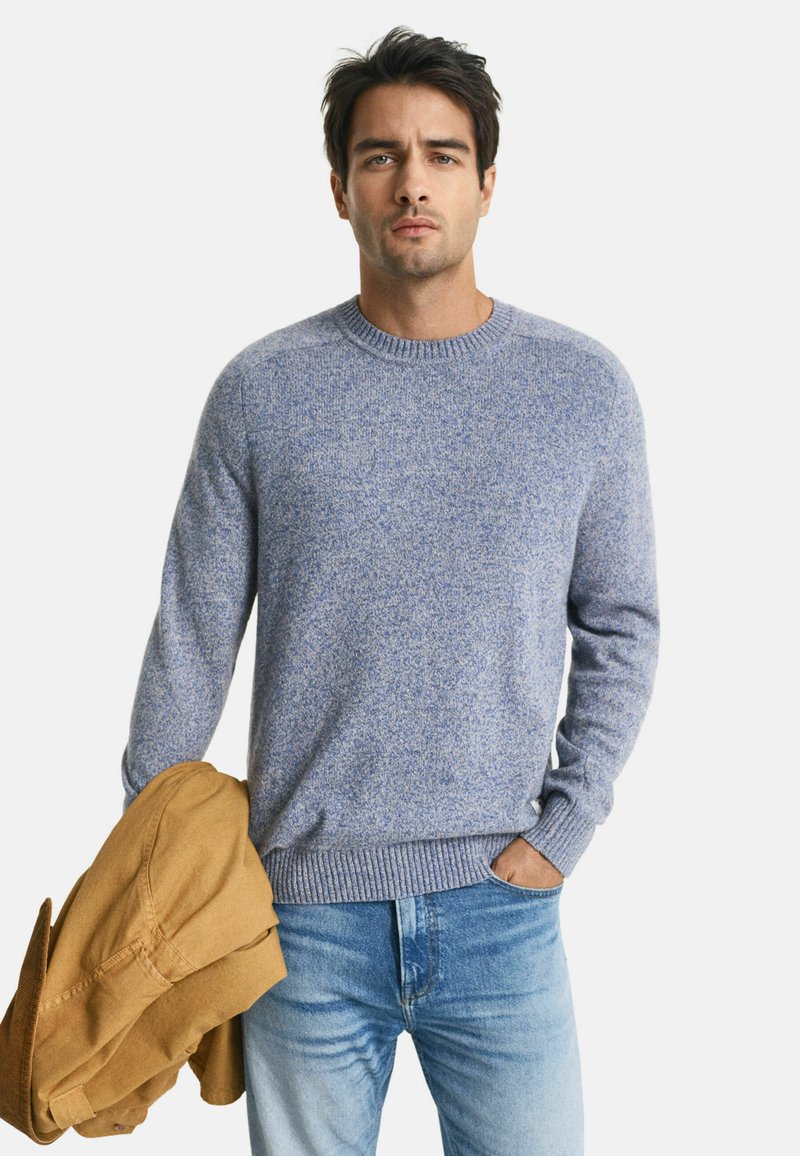 Blauer Pullover mit strukturiertem Muster. Runder Ausschnitt, gerippte Bündchen und Saum. Getragen mit hellblauen Jeans und einer braunen Jacke.