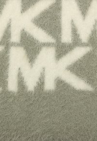 Graues Textil mit einer weichen, fusseligen Textur, das mutige, weiße Buchstaben und Muster von "MK" auf der Oberfläche zeigt, die miteinander verwoben sind.