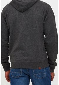 Szary bawełniany hoodie z kapturem na sznurki, rękawami raglanowymi i ściągaczem na dole, w połączeniu z niebieskimi dżinsami z charakterystycznymi wzorami stębnowania.