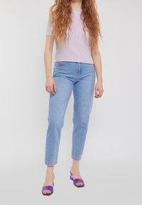 Top corto de manga corta de rayas en púrpura claro, combinado con jeans rectos de pierna azul claro y sandalias de tacón bloque transparente en púrpura.