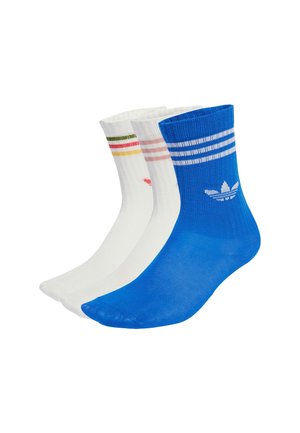 Tre paia di calzini: uno blu con strisce bianche e logo, uno bianco con strisce rosa e verdi, e uno bianco puro con un piccolo design.