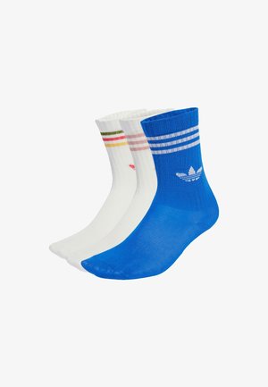 Tre paia di calzini: uno blu con strisce bianche e logo, uno bianco con strisce rosa e verdi, e uno bianco puro con un piccolo design.