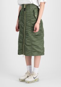 Gonna midi verde imbottita con zip frontale, tasche laterali e vita arricciata. Indossata con calze bianche e scarpe con dettagli neri.