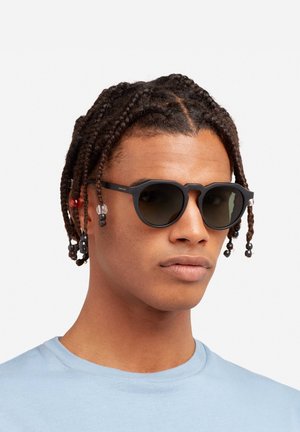 Akiniai nuo saulės su juodais rėmeliais ir tamsiais lęšiais. Išsiskiria unikalia išpjovų forma, struktūruotais guitaromis ir dekoratyviniais karoliukais.