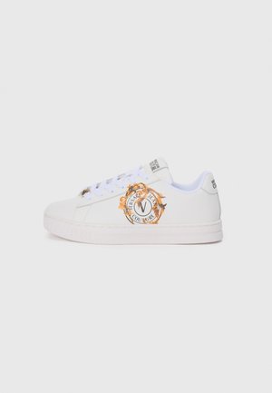 Hvit sneaker laget av glatt lær med et sirkulært oransje og svart logo-design. Snøring og strukturert gummisåle.