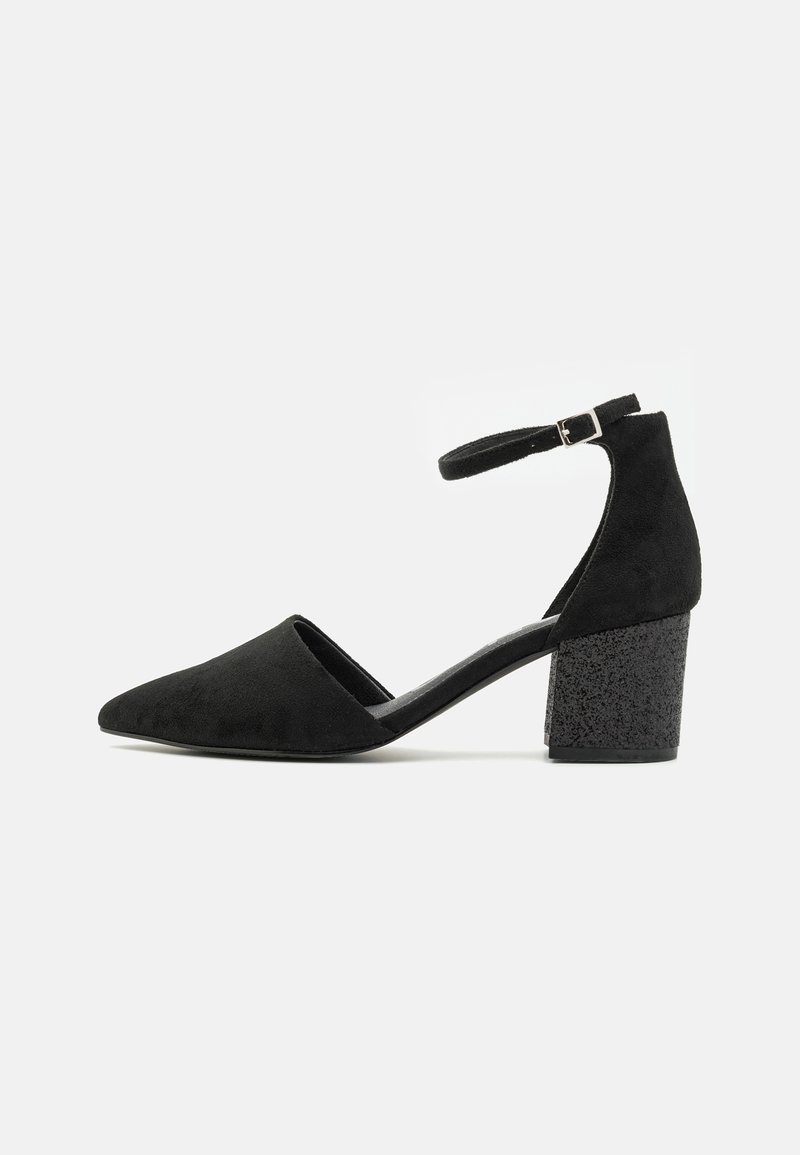Tacones altos de ante negro con tiras en el tobillo, punta afilada y tacón grueso texturizado. Presenta un interior suave y una correa ajustable.