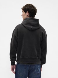 Μεγάλο φούτερ σε σκούρο γκρι χρώμα από μαλακό ύφασμα, με μεγάλο κουκούλι, χαμηλωμένους ώμους και ριμπ μανσέτες. Φοριέται με μπλε τζιν παντελόνι.