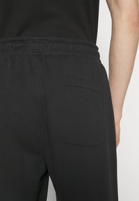 Zwarte trainingsbroek met een elastische tailleband en achterzak, met een gladde textuur en een eenvoudig ontwerp.