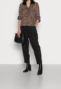 Leopardi-kuosiset puserot, jossa on V-kaula-aukko ja 3/4-hihat, yhdistettynä korkeavyötäröisiin mustiin housuihin ja polven ylle ulottuviin mustiin nahkasaappaisiin.