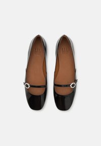Balerini din piele la patină neagră cu vârful pătrat, având o curea decorativă și un embellisment asemănător cu cristalul pe o parte.