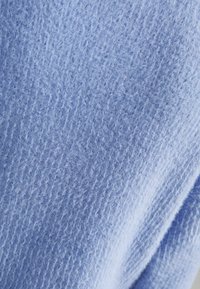 Měkká tkanina v světle modré barvě, s jemným žebrovaným vzorem. Materiál vypadá nadýchaně a útulně, s mírně nerovným povrchem.