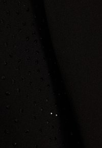 Gros plan sur un tissu noir avec une couture diagonale, orné de petites perles noires brillantes sur un côté.