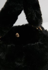 Okrągła czarna torebka z imitacji futra o miękkiej fakturze, wyposażona w gruby uchwyt i złote akcenty metalowe przy zapięciu.