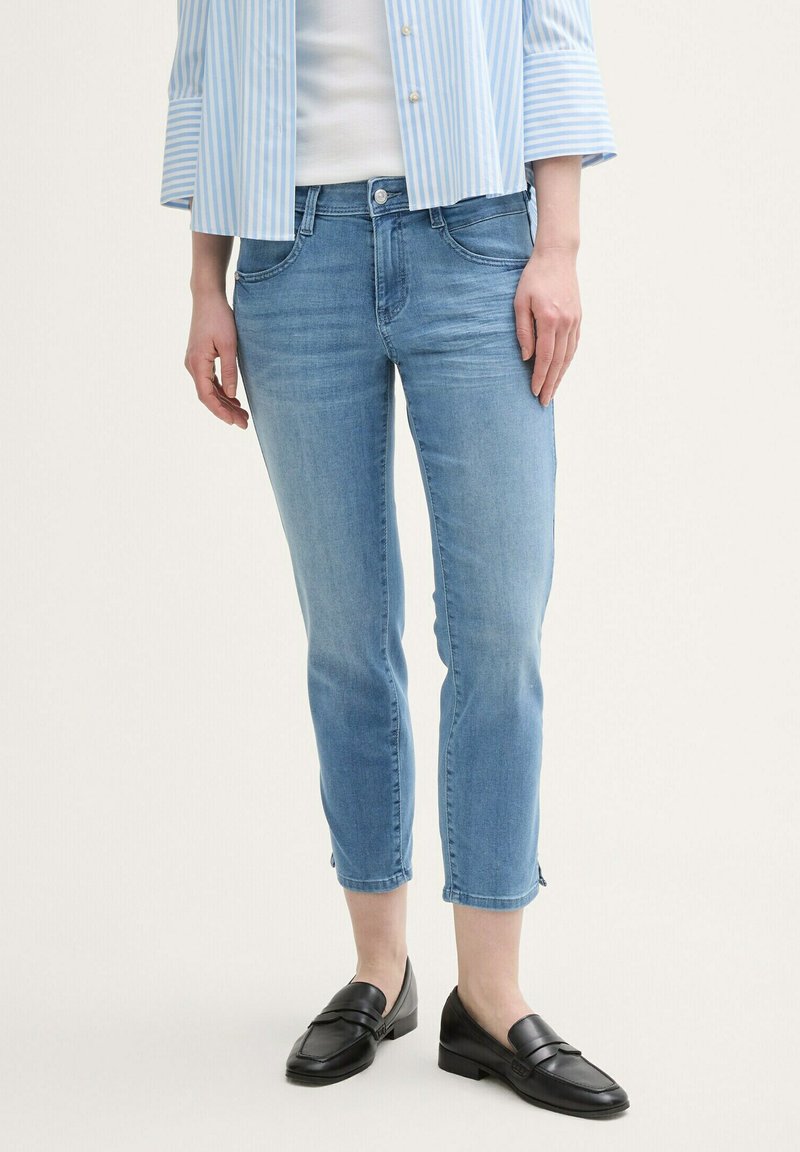 Gaiši zili džinsa īsie džinsi ar vieglu izbalējumu, piecu kabatu dizains un saplēsts apakšmalas mala. Saskaņoti ar melniem loaferiem un svītrainu zilu kreklu.