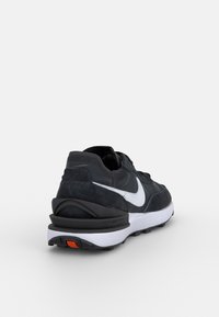 Nike teniska v tmavě šedé barvě s bílým logem Swoosh. Má texturovaný svršek, polstrovaný límec a černo-bílou podrážku s oranžovým akcentem.