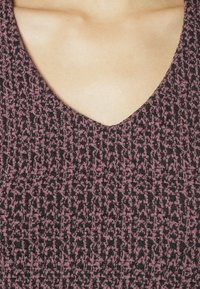 Top a V con un tessuto testurizzato e a fantasia che presenta tonalità di nero e rosa polveroso, mostrando la pelle sul décolleté.