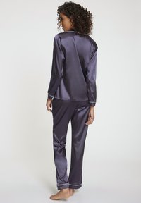 Satin-Pyjama-Set in tiefem Lila, mit langen Ärmeln und Hosen, ausgestattet mit einem weißen Paspelkragen und -bündchen. Glatte Textur, lockere Passform.