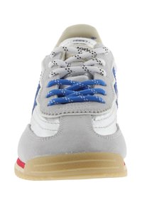 Zapatilla gris y blanca con cordones azules y blancos, suela de goma y detalle lateral azul, vista desde un ángulo frontal.