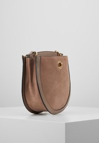 Borsa a mano in suede marrone con una forma arrotondata, rifiniture nere e dettagli in oro. Caratterizzata da una tracolla singola per il trasporto.