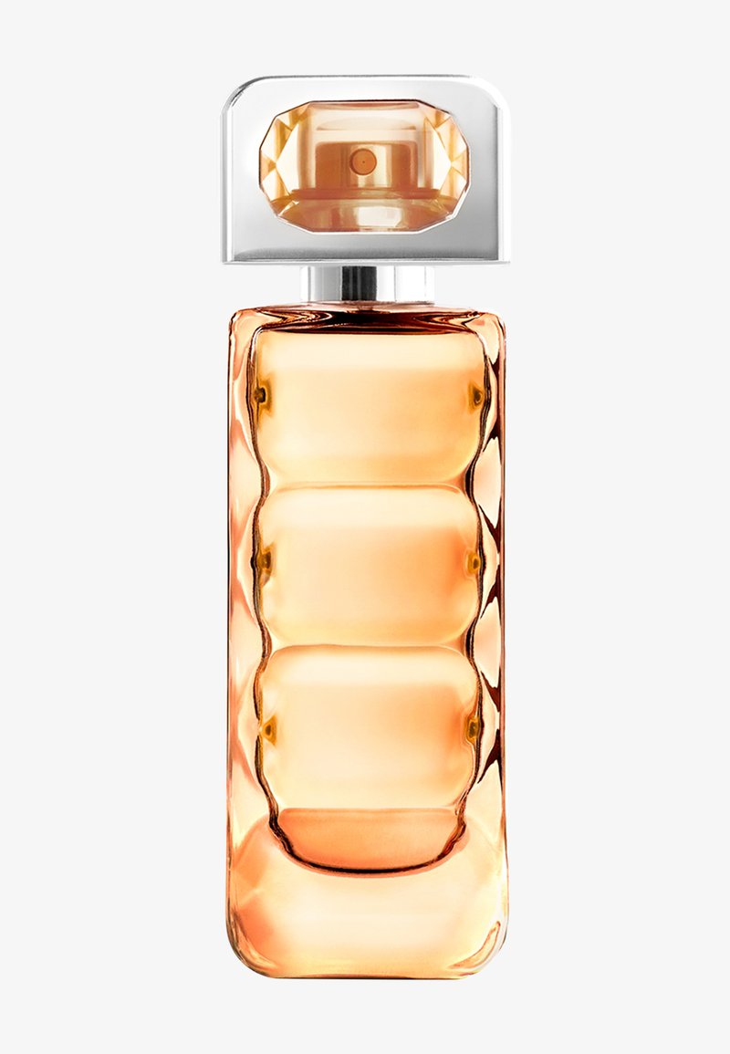 Flacon de parfum rectangulaire et haut avec un liquide ambré clair et un bouchon pulvérisateur argenté facetté sur le dessus.