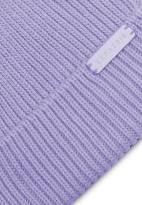 Gorro de lana color lavanda con textura de canalé. Presenta una etiqueta de marca de color púrpura claro cosida en la tela. Material suave y elástico.