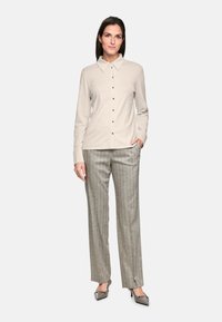 Beige long-sleeve shirt with a collar and front buttons, paired with gray striped trousers, and pointed gray heels. Smooth fabric texture.