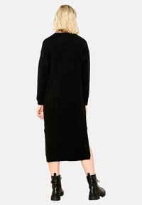 Lång svart stickad klänning med långa ärmar, rund halsringning och sidofack, i kombination med svarta klumpiga klackstövlar. Mjuk textur.