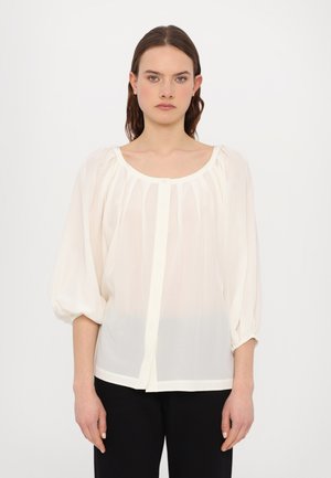Lichte, doorschijnende crèmekleurige blouse met een ronde halslijn, puffmouwen en verticale plooien. Bevestigd met een knop aan de voorkant.