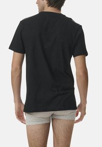 Black cotton t-shirt with a round neckline, short sleeves, and relaxed fit, worn with light gray underwear, displaying a simple design.