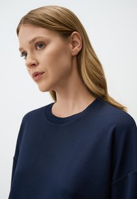 Sweatshirt in cotone navy con scollo rotondo e finiture a costina. Presenta spalle scese e una vestibilità rilassata, con una texture liscia.